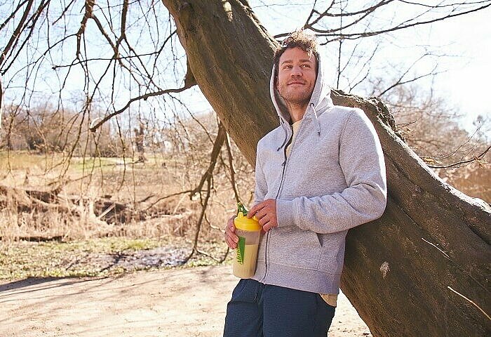 Sportlicher Mann im Park mit einem Almased Shake mit hoher biologischer Wertigkeit in der Hand.