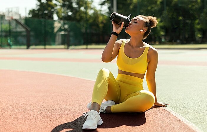 Frau-trinkt-Proteinshake-auf-Sportplatz-um-Stoffwechsel-anzuregen