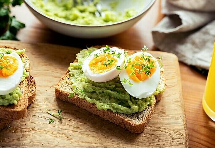 Brot mit Erbsenaufstrich und Eiern auf einem Holzbrett als Mahlzeit mit einer hohen biologischen Wertigkeit.