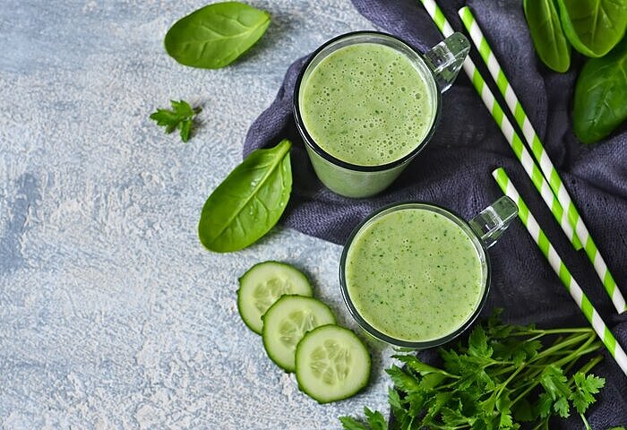 Grüner Abnehmshake mit Gurke, Spinat und grünen Strohhalmen in zwei Gläsern